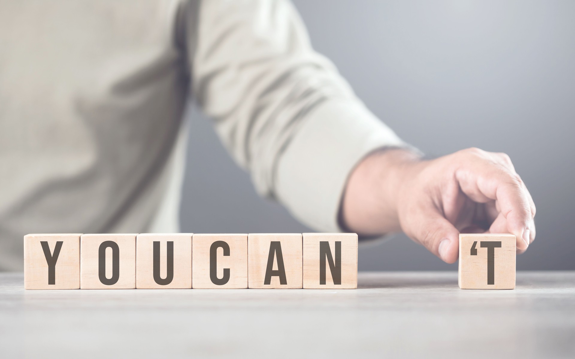 Hand separates the letter T from the word you can't transforming it into can. The image symbolizes overcoming obstacles, shifting from doubt to empowerment, and embracing a positive mindset