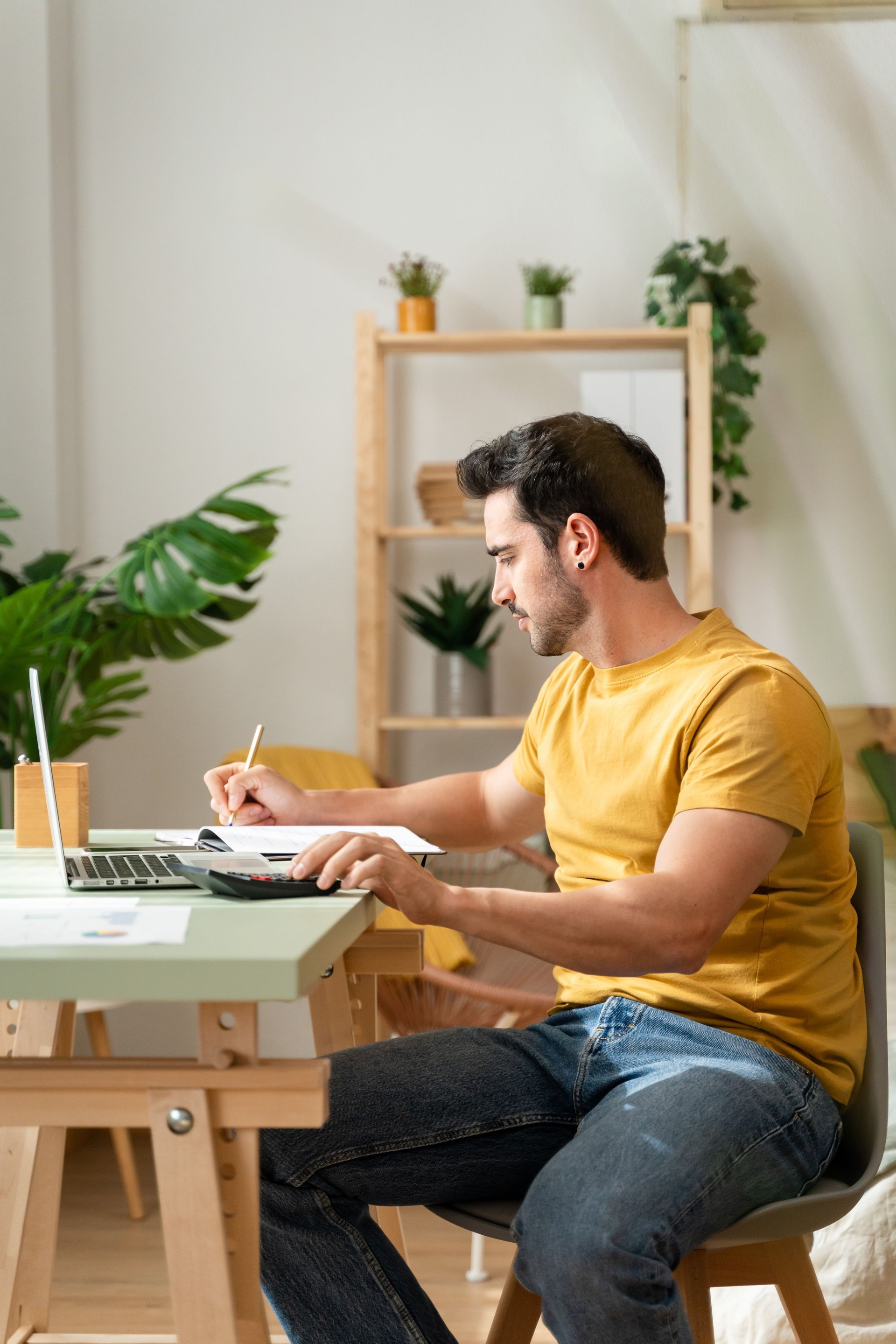 Man sitting at desk at home doing bills with calculator.