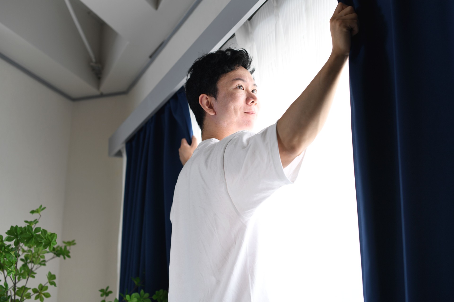 Asian man opening the curtains and soaking in the sunlight
