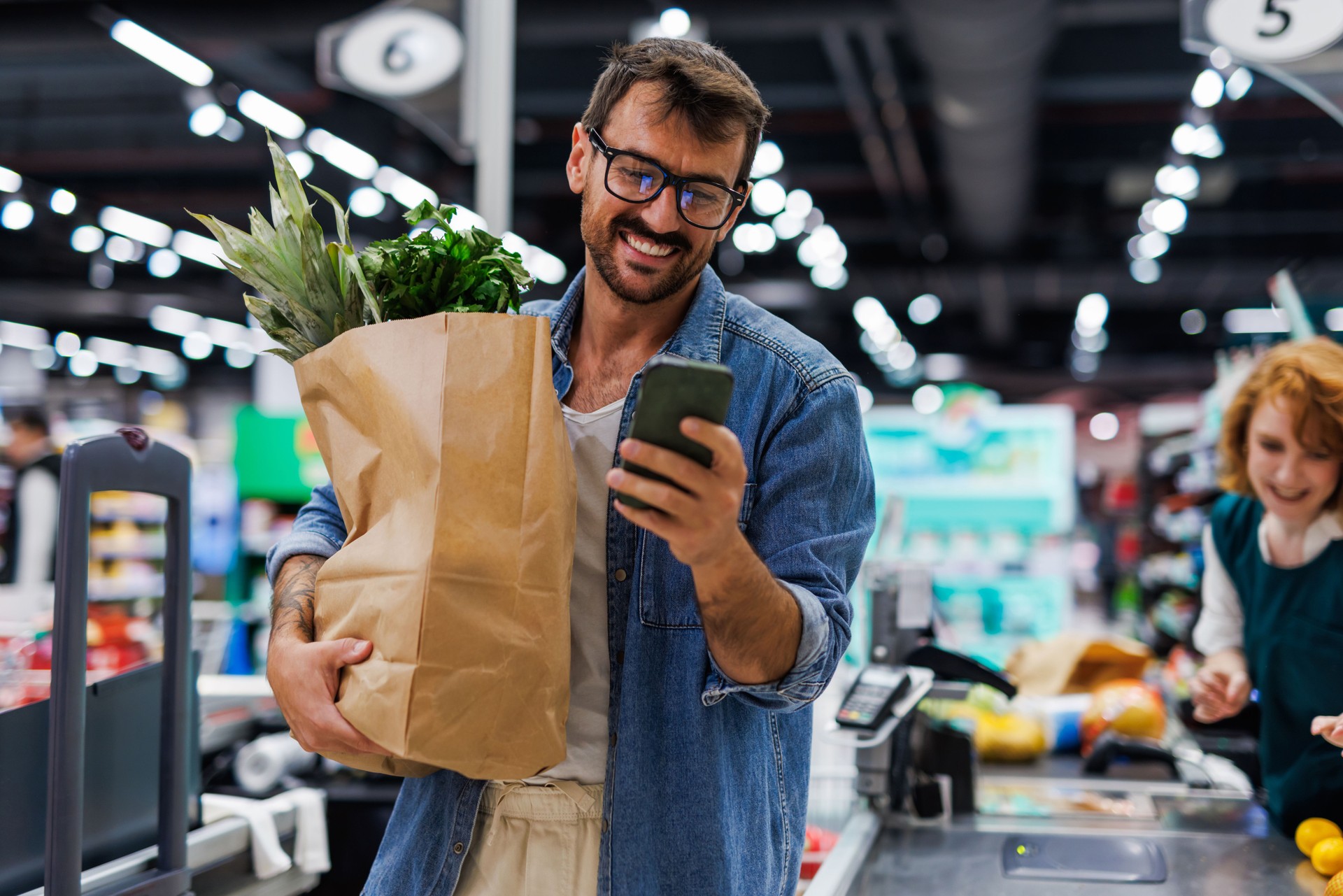 Smiling customer using smartphone while holding grocery bag at checkout