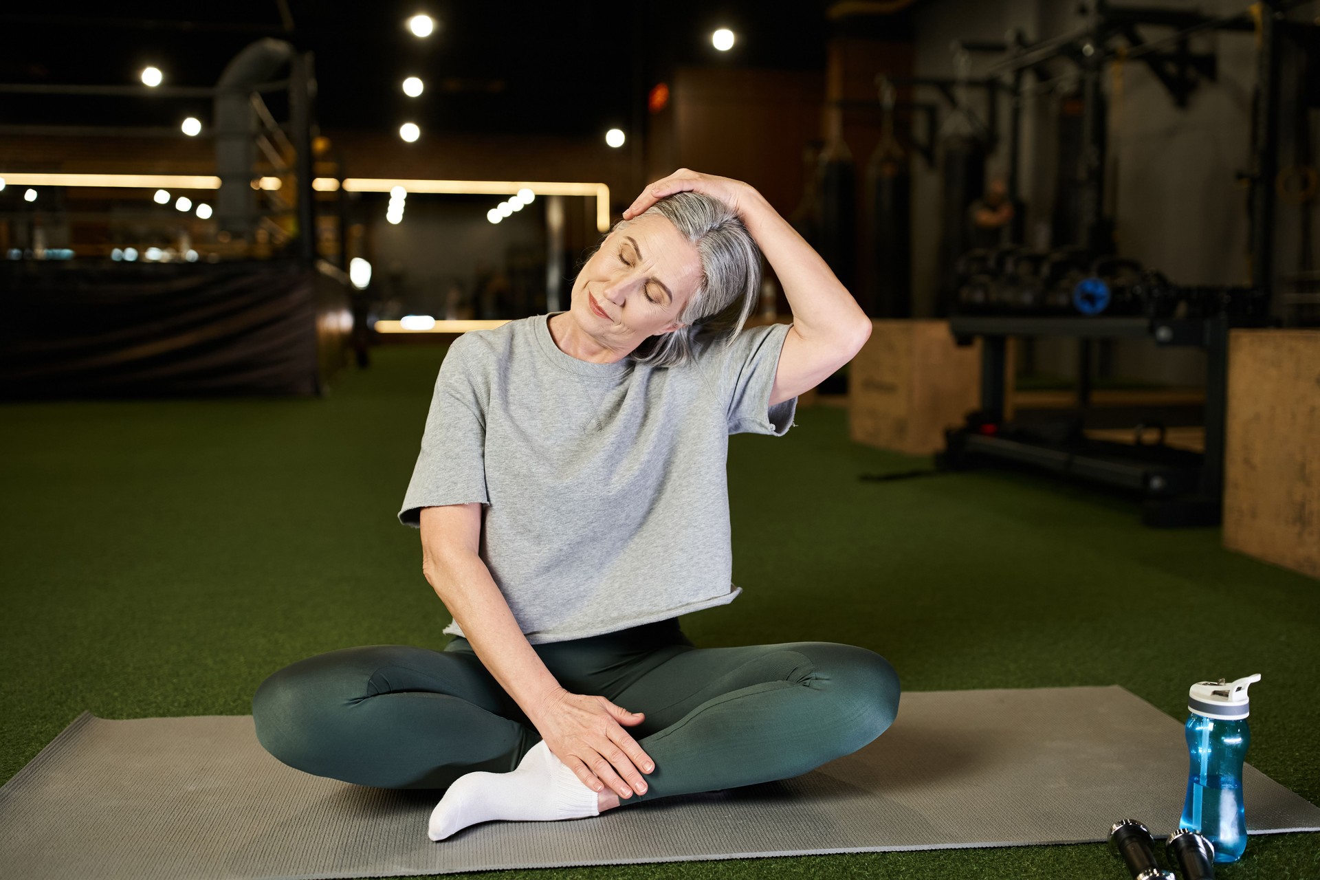 Active senior woman with grey hair stretches in a vibrant gym during her fitness routine