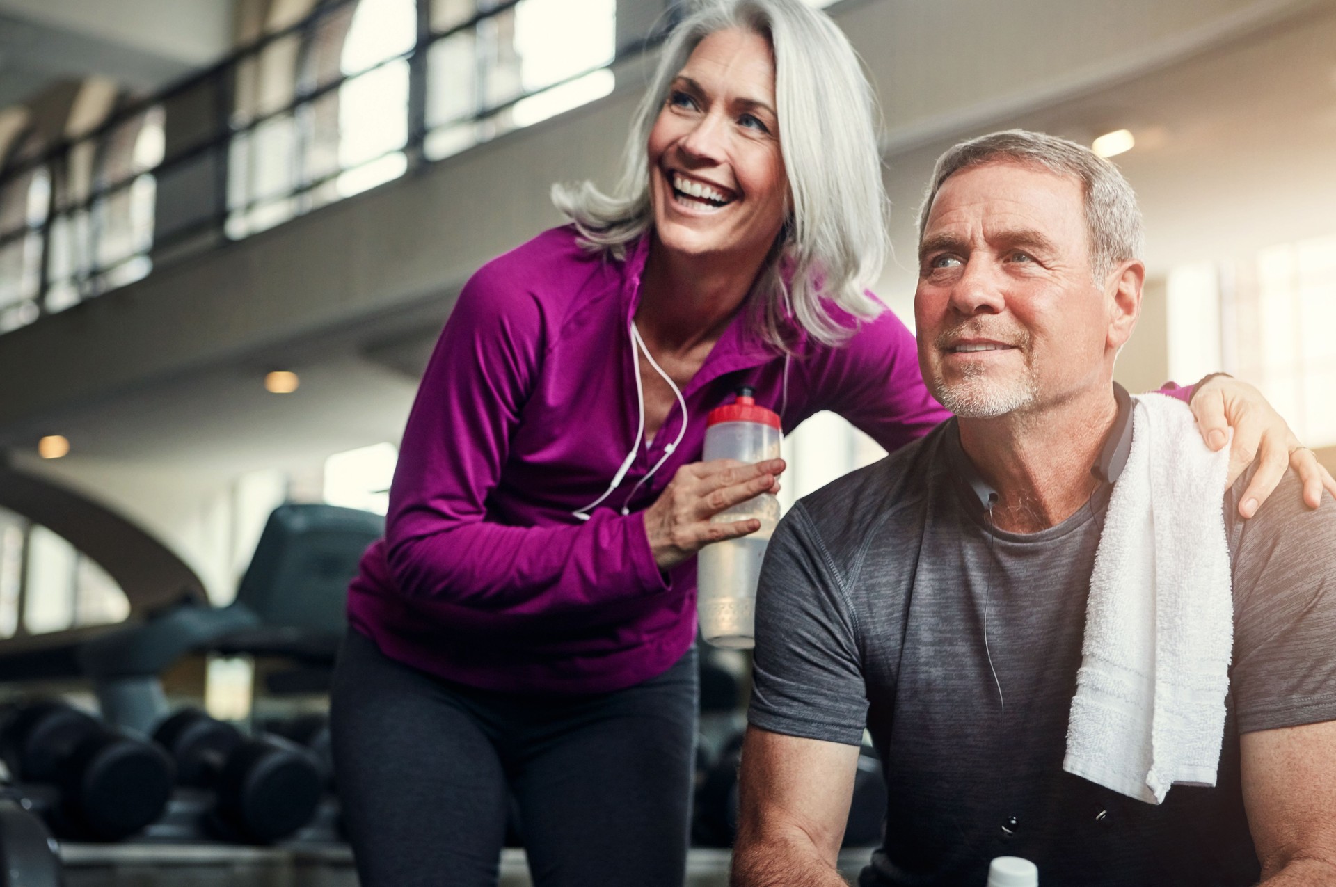 Happy, fitness and mature couple at a gym for water, break or bonding after morning, cardio or performance. Workout, support or sports people resting at exercise studio for wellness, care or training